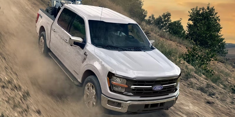 White Ford F-150 pickup truck driving on a dusty off-road trail, showcasing its capability, durability, and performance in rugged terrain