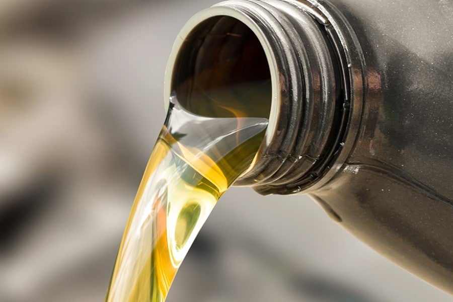 Close-up of fresh motor oil being poured from a container, illustrating an engine oil change and vehicle lubrication service